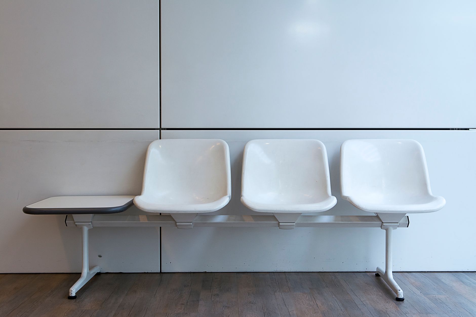 A row of empty white waiting room seats with a small side table against a pale wall